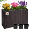 A brown rattan-style planter with three different types of flowers and three black pots below. Produktbild-Vorschau