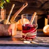 A glass of mulled wine with cinnamon sticks and orange slices, next to a copper pot and ladle. Anteprima dell’immagine prodotto