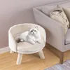 A cat is resting on a raised pet sofa next to a larger sofa. Produktbild-Vorschau