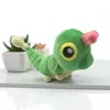 A plush toy caterpillar is placed on a white surface with blurred potted plants in the background. Produktbild-Vorschau
