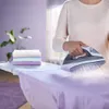 A person is ironing clothes on an ironing board, with a stack of folded laundry next to them. Voir les images du produit