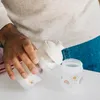 A person is pouring milk powder from a dispenser into a baby bottle. Produktbild-Vorschau