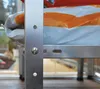 A close-up view of a silver plant stand with a white and orange bagged item on it. Náhľad obrázku produktu