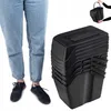 A person's legs and feet are shown on the left, wearing jeans and black sneakers. To the right, a stack of black plastic trash bins with lids is displayed. Podgląd zdjęcia produktu