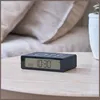 A digital alarm clock sits on a wooden table next to a plant. Produktbild-Vorschau