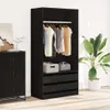 A black wardrobe with clothes hanging inside and drawers at the bottom, placed next to a chest of drawers and a potted plant. Anteprima dell’immagine prodotto