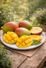 A plate of sliced and whole mangoes on a wooden table outdoors. Podgląd zdjęcia produktu