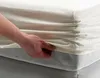 A hand is shown tucking a white fitted sheet onto a mattress. Produktbild-Vorschau