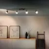 A modern living room with a track light fixture illuminating artwork and a cabinet. Produktbild-Vorschau