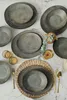 A collection of ceramic plates and bowls arranged on a marble surface, with cutlery and glasses. Anteprima dell’immagine prodotto
