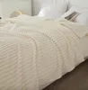 A close-up view of a cream-colored blanket with a textured pattern, draped over a bed. Podgląd zdjęcia produktu