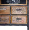 A close-up view of a vintage-style apothecary cabinet with multiple drawers, some featuring decorative patterns and metal handles. A framed invitation or announcement is visible at the top. Podgląd zdjęcia produktu