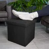 A person's feet in socks resting on a black ottoman in a living room setting. Náhled obrázku produktu