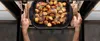 Hands are shown removing a roasting pan filled with roasted potatoes from an oven. Produktbild-Vorschau