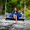 A woman sits on a swing over a river, wearing a blue dress. Náhled obrázku produktu