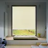 A roller blind is installed on a large window, partially covering the view of a grassy outdoor area. A mattress-like cushion is placed on a wooden platform in front of the window. Náhled obrázku produktu