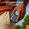 A hand is holding a dark blue power bank, placing it into the pocket of light-colored pants. The background shows greenery and a blue sky. Produktbild-Vorschau