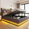 A modern bedroom with a bed that has its storage compartment open, revealing items inside. The bed has LED lighting around its base. Voir les images du produit