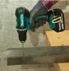 A person wearing gloves is using a cordless drill to drill into a metal bar, which is resting on a wooden surface. Produktbild-Vorschau