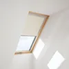 A skylight window with a beige roller blind partially covering it, set against a white sloped ceiling. Produktbild-Vorschau