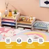 A desk organizer with multiple shelves filled with office supplies and stationery, set against a pink and white background with a cartoonish rainbow and mouse design. Produktbild-Vorschau