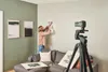 A person is hanging a picture on a wall while a tripod with a laser level is set up in the foreground. Podgląd zdjęcia produktu