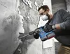A man is using a Bosch rotary hammer to break apart a tiled wall. Voir les images du produit