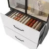 A close-up view of an open drawer in a white cabinet, revealing neatly folded items organized in compartments. The cabinet has a glass top, showing more items inside. Podgląd zdjęcia produktu