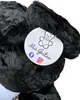 A close-up view of a black teddy bear's ear and a tag with branding and social media icons. Podgląd zdjęcia produktu