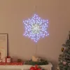 A snowflake-shaped light decoration hangs on a wall above a shelf with Christmas gifts and candles. Produktbild-Vorschau