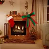 A decorated fireplace with a Christmas stocking, a small Christmas tree, and a large red and green bow. Produktbild-Vorschau