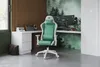 A gaming chair is set up in a modern gaming room with a desk, computer, and nature-themed wallpaper. Produktbild-Vorschau