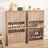 Two wooden shoe cabinets are shown in a room, one slightly in front of the other. The cabinets have slatted doors and open shelves displaying shoes. A lamp, radio, and plant are on top of the left cabinet. A gift-wrapped box and stool are to the left of th Voir les images du produit