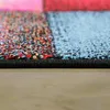 A close-up, side view of a colorful, geometric patterned rug with a black edge, resting on a wooden floor. Produktbild-Vorschau