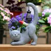 A garden decoration featuring a cat statue with a gnome holding a lantern on its back, surrounded by flowers. Produktbild-Vorschau