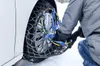 A person is installing snow chains on a car tire in a snowy environment. Náhľad obrázku produktu