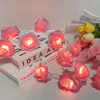 A string of pink rose-shaped LED lights is draped over two books, with a bouquet of yellow and white tulips in the background. Produktbild-Vorschau