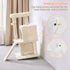 A beige cat tree with two houses, sisal scratching posts, and a toy ball, shown in a room with curtains and a wall. Close-up insets show how the anti-tip device attaches to the wall. Produktbild-Vorschau