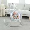 A baby is sitting in a baby swing in a living room. Produktbild-Vorschau