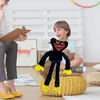 A child is holding a black plush toy with yellow feet and hands, smiling at a person holding a clipboard. The setting appears to be a therapy or play session. Produktbild-Vorschau