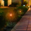 Solar garden lights with a flame effect illuminate a pathway and garden at dusk. Náhled obrázku produktu