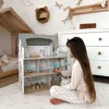 A young girl plays with a wooden dollhouse in a child's room. Voir les images du produit