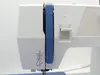 A close-up view of the side of a white sewing machine with blue accents. Náhľad obrázku produktu