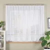 A white lace curtain hangs in a window, with a wooden windowsill visible below. A white shelf unit with decorative items is to the left, and a potted plant with large leaves is to the right. Náhled obrázku produktu
