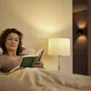 A woman is reading a book in bed, illuminated by a bedside lamp. Anteprima dell’immagine prodotto
