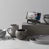 A smartphone is charging on a stand, displaying a video of people in a kitchen. Produktbild-Vorschau
