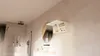 A modern bathroom with a wall-mounted cabinet open, displaying toiletries, next to a round mirror and a sink. Produktbild-Vorschau