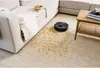 A robot vacuum cleaner is cleaning up spilled chips on a carpet next to a sofa and a coffee table. Produktbild-Vorschau