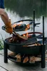 A person is grilling a large piece of meat over a fire pit by a lake. Náhled obrázku produktu