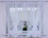 A white sheer curtain with lace trim is hung on a window. Náhled obrázku produktu